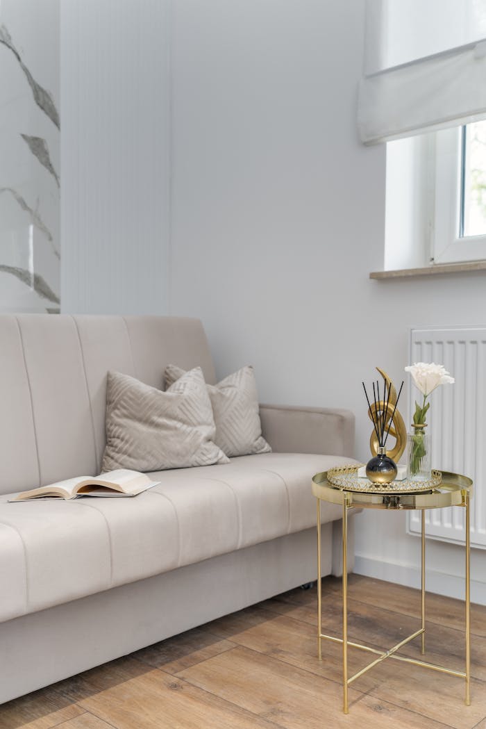 gallery-1 Stylish interior with beige sofa, pillows, and a gold coffee table beside a window.